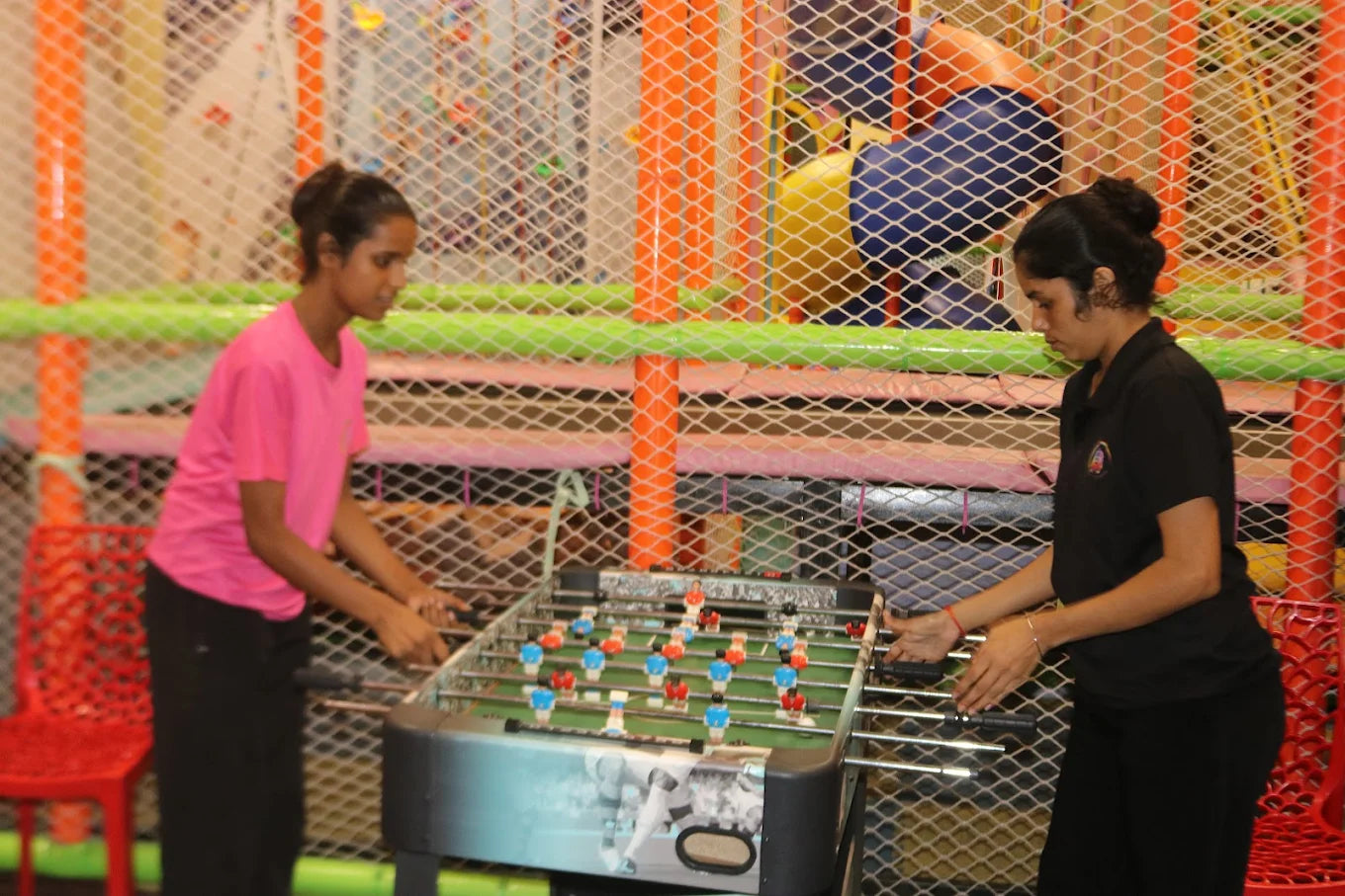 Two girls focused on playing foosball inside a vibrant indoor kids play area with colorful climbing equipment