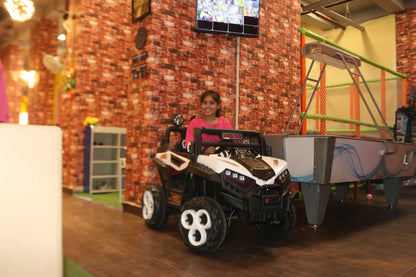 Child in a toy car in an indoor play area with brick wall and toys.