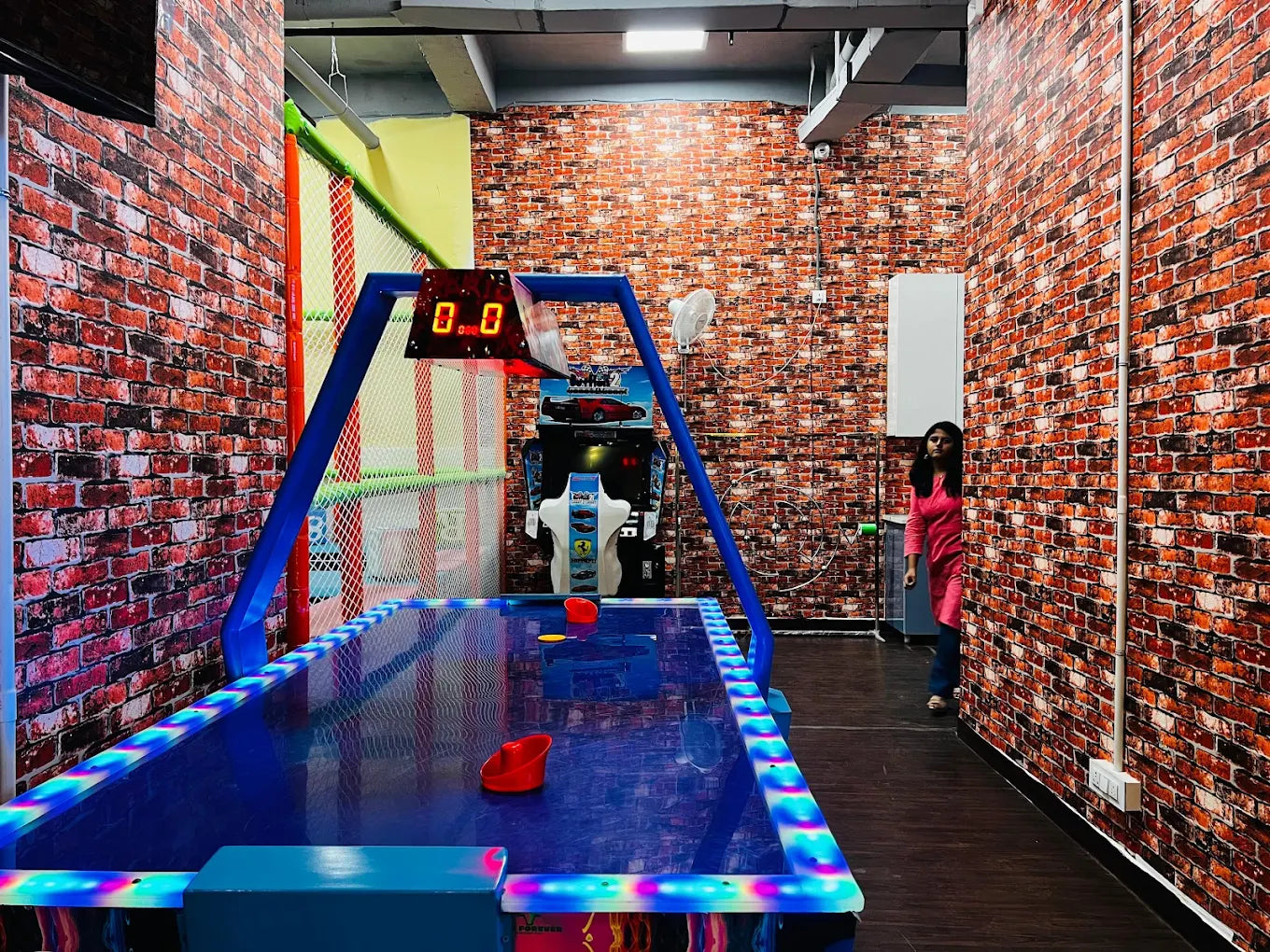 Indoor game room featuring an illuminated air hockey table set against brick-patterned walls and dark flooring