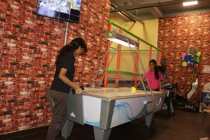 Two people playing air hockey in a room with brick walls and a TV.