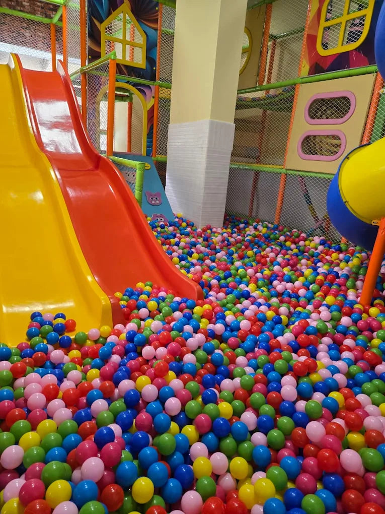 Brightly colored double slides descending into a large ball pit filled with multicolored plastic balls in an indoor play area