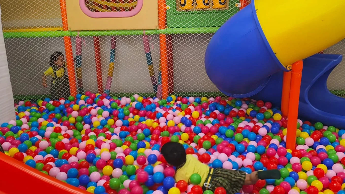 Children playing in a ball pit with colorful balls and a slide in an indoor playground.