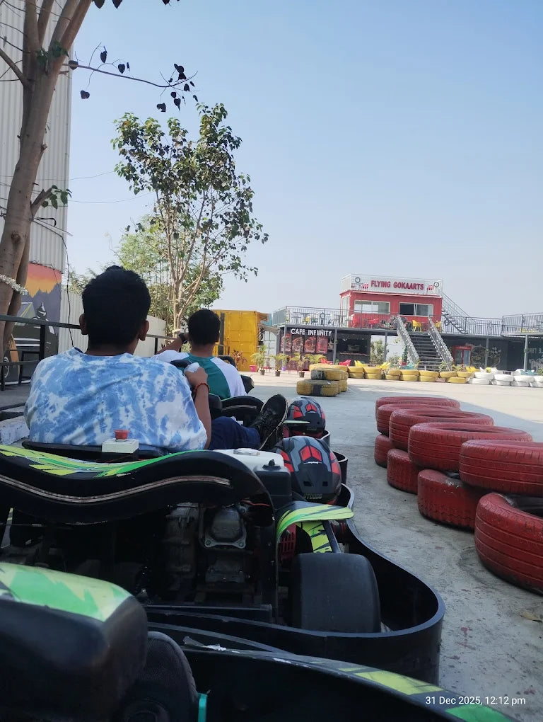 Two young people in go-karts at an outdoor track, with a building labeled "FLYING GOKARTS" in the background.