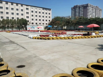 A go-kart track with tire barriers and two red umbrellas, with buildings in the background.