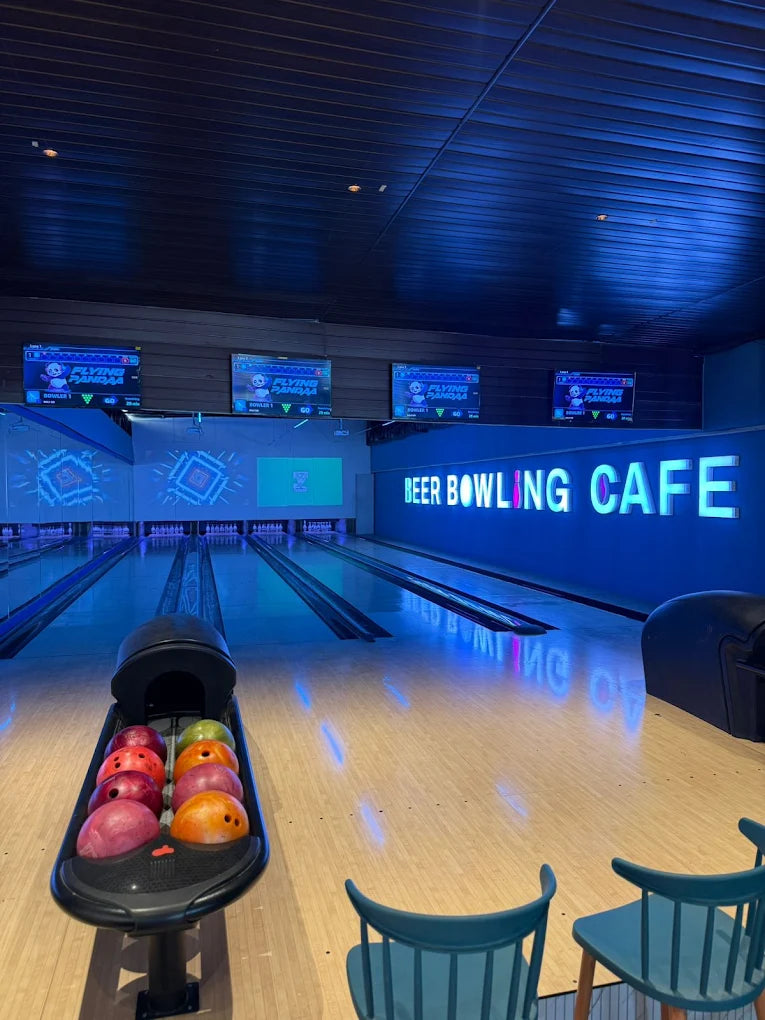 A bowling alley with neon lights and bowling balls in a rack.