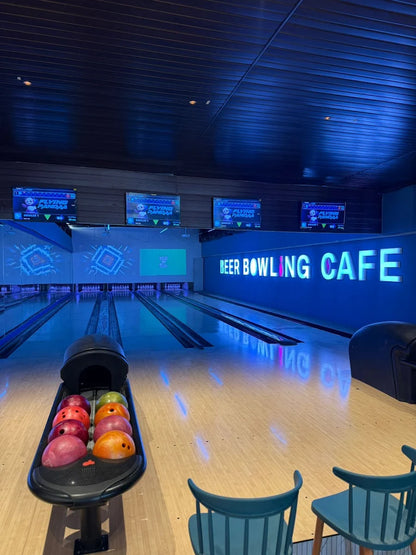 A bowling alley with neon lights and bowling balls in a rack.