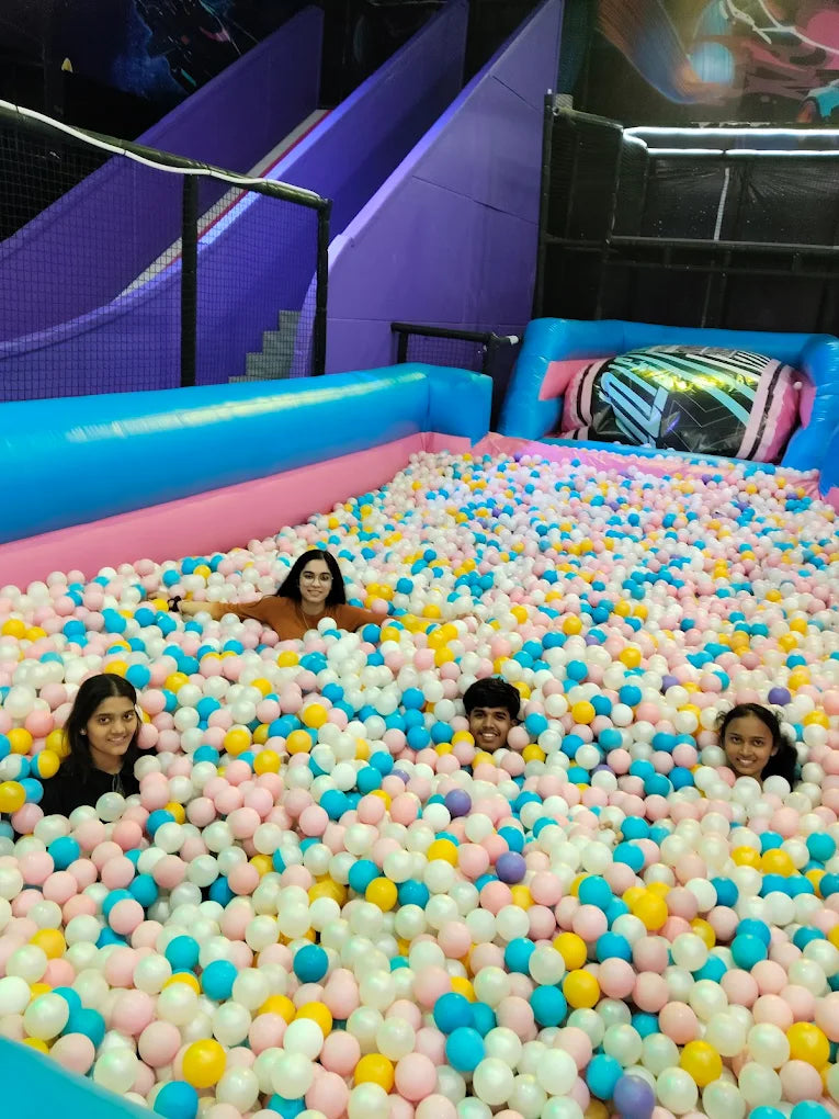 Four young people are playing in a ball pit at an indoor playground.