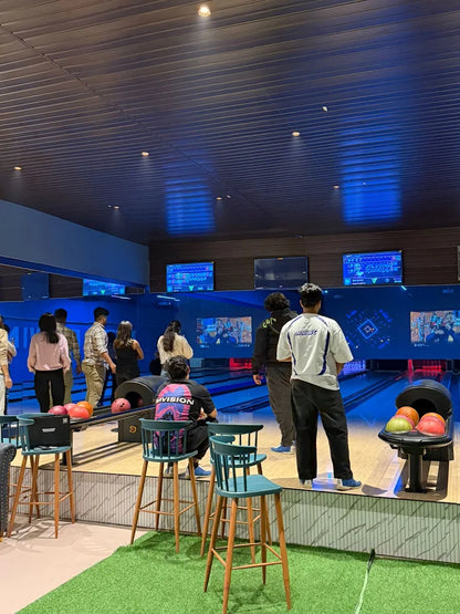 Young adults bowling in a modern alley with blue lighting.