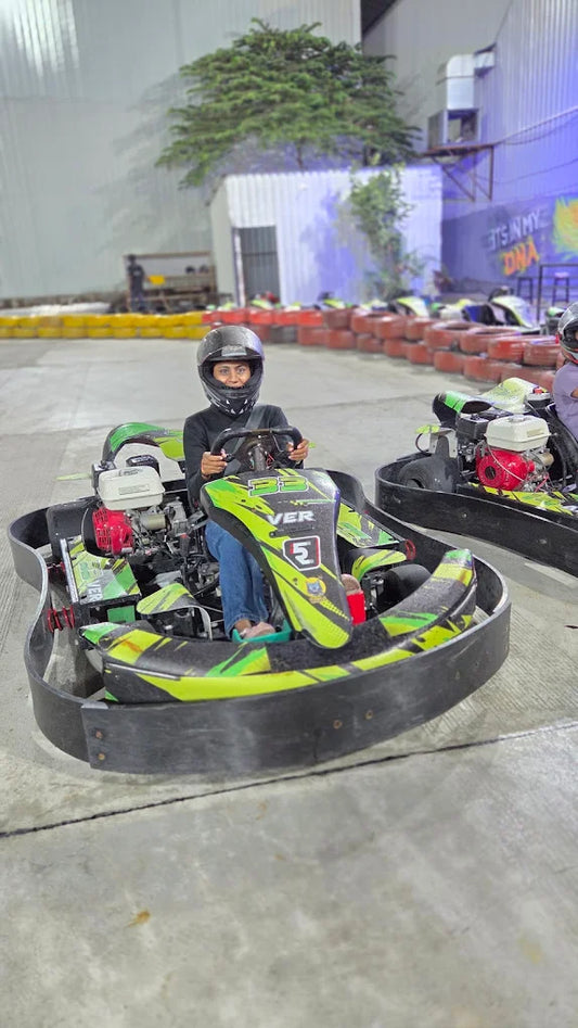 A young person in a helmet sits in a go-kart on a track.