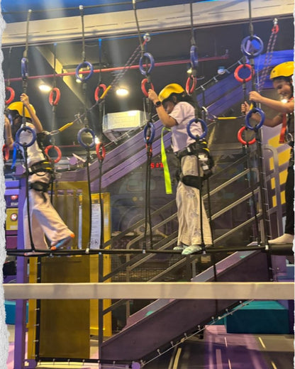 Children navigating an indoor ropes course with harnesses and safety equipment.