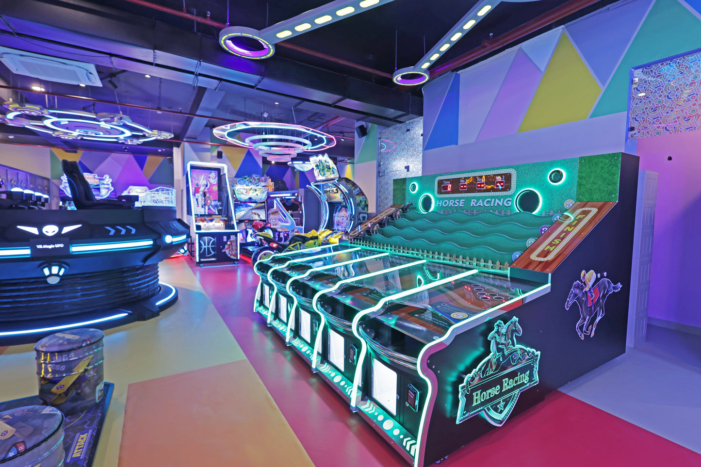 An arcade with colorful lights and various games, including a horse racing machine and a VR UFO ride.