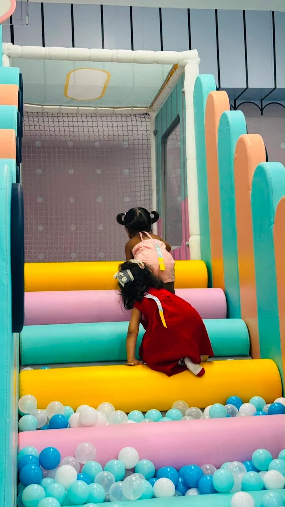 Two young children play in a colorful indoor playground with a ball pit.