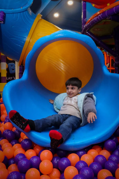 Young boy exiting yellow and blue spiral slide into vibrant ball pit at Fun Orbbit Kids Play Area Gujranwala Town Delhi
