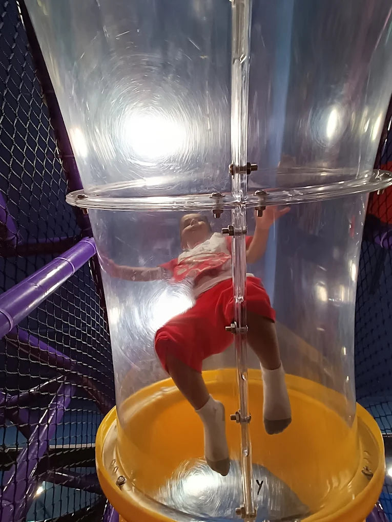 Child wearing red shorts plays inside transparent vertical tube slide at Fun Orbbit Kids Play Area Gujranwala Town Delhi