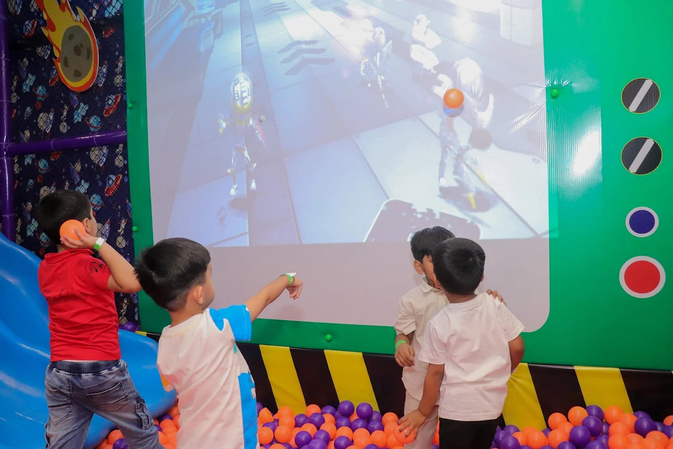 Four children throwing orange balls at an interactive screen above a purple and orange ball pit at Fun Orbbit Gujranwala Town Delhi