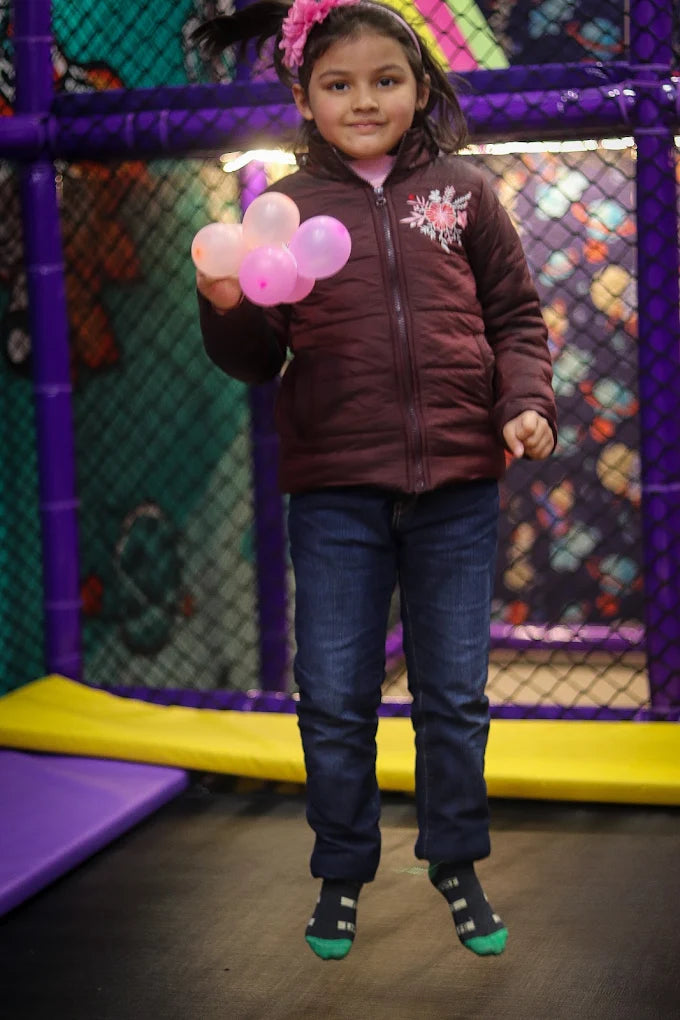 Young girl holding pink balloons while jumping in indoor play area with purple netted walls at Fun Orbbit Gujranwala Town