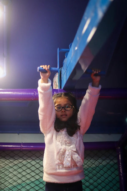 Girl with glasses gripping blue monkey bars inside indoor play area at Fun Orbbit Kids Play Area Gujranwala Town Delhi