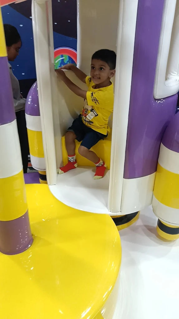 Smiling boy in yellow shirt riding colorful rotating play equipment at Fun Orbbit Kids Play Area Gujranwala Town Delhi