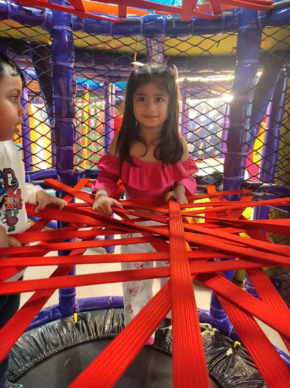 Girl in pink top exploring web of red ropes in colorful netted play structure at Fun Orbbit Kids Play Area Gujranwala Town Delhi