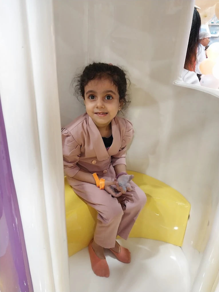 Young girl in light pink outfit sitting inside a white play structure with yellow seat at Fun Orbbit Kids Play Area Gujranwala Town Delhi