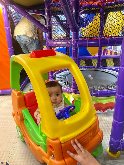 Toddler sitting inside colorful plastic toy car in vibrant play area with purple climbing structure at Fun Orbbit Gujranwala Town Delhi