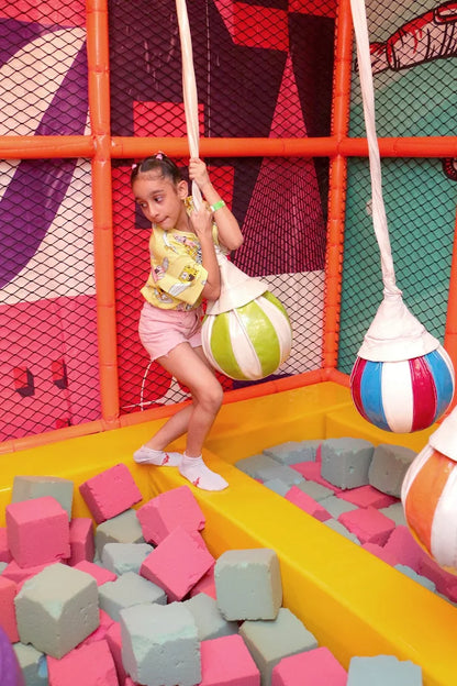 Young girl balancing on green and white swinging ball above foam block pit inside colorful play area at Fun Orbbit Gujranwala Town Delhi