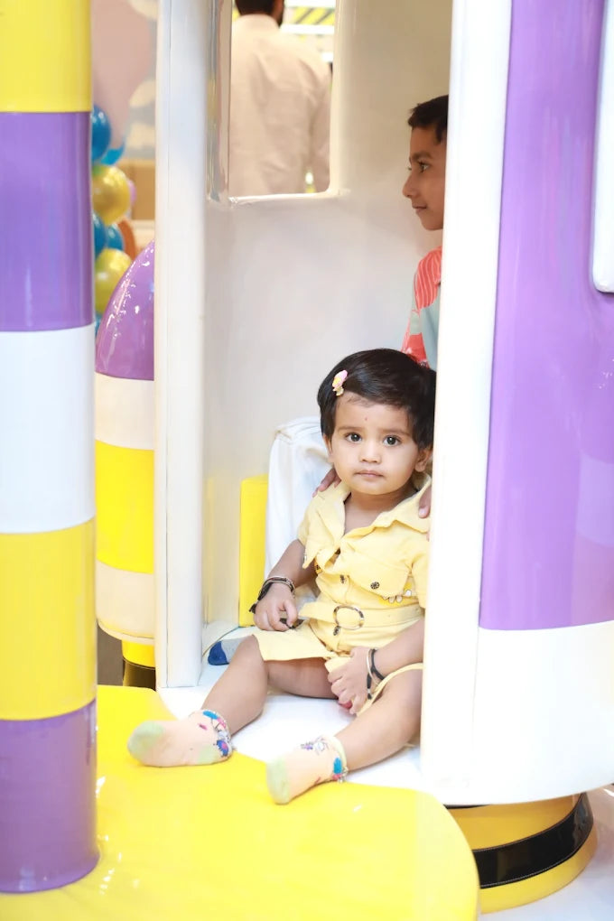 Toddler in yellow dress sitting inside white and purple play structure with boy in background at Fun Orbbit Kids Play Area Gujranwala Town Delhi