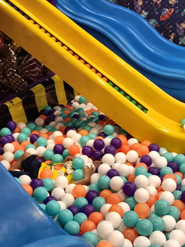 Child partially hidden under multicolored plastic balls near yellow and blue slides in vibrant Fun Orbbit play area Gujranwala Town Delhi