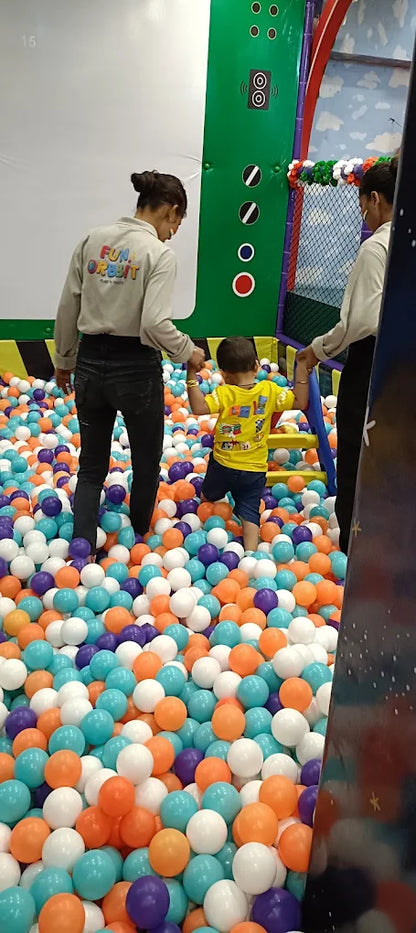 Child in yellow shirt walking through multicolored ball pit with two adults holding their hands at Fun Orbbit Gujranwala Town Delhi
