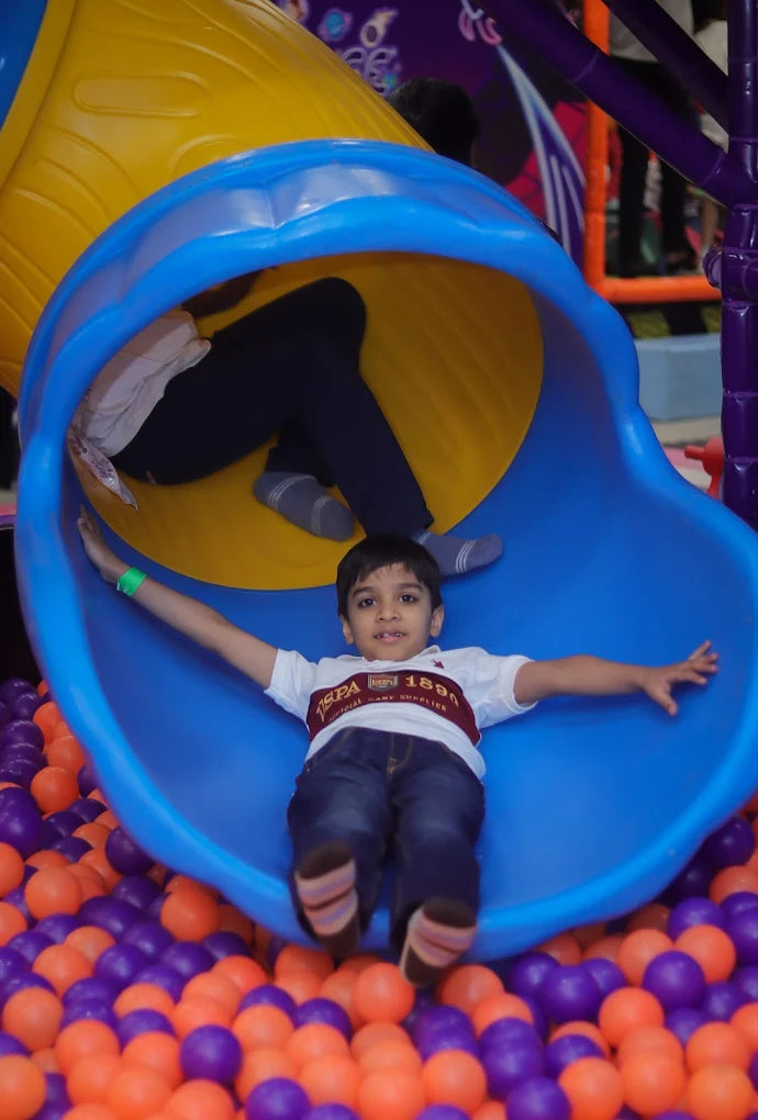Boy sliding down wide blue tunnel slide into orange and purple ball pit at Fun Orbbit Kids Play Area Gujranwala Town Delhi