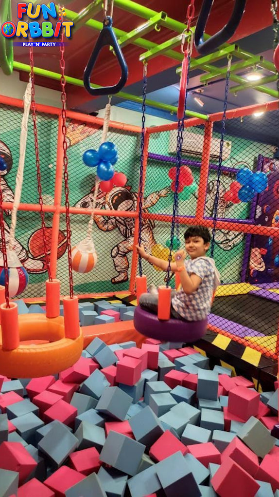 Child sitting on purple swing over foam cube pit with space-themed murals in Fun Orbbit Kids Play Area Gujranwala Town Delhi