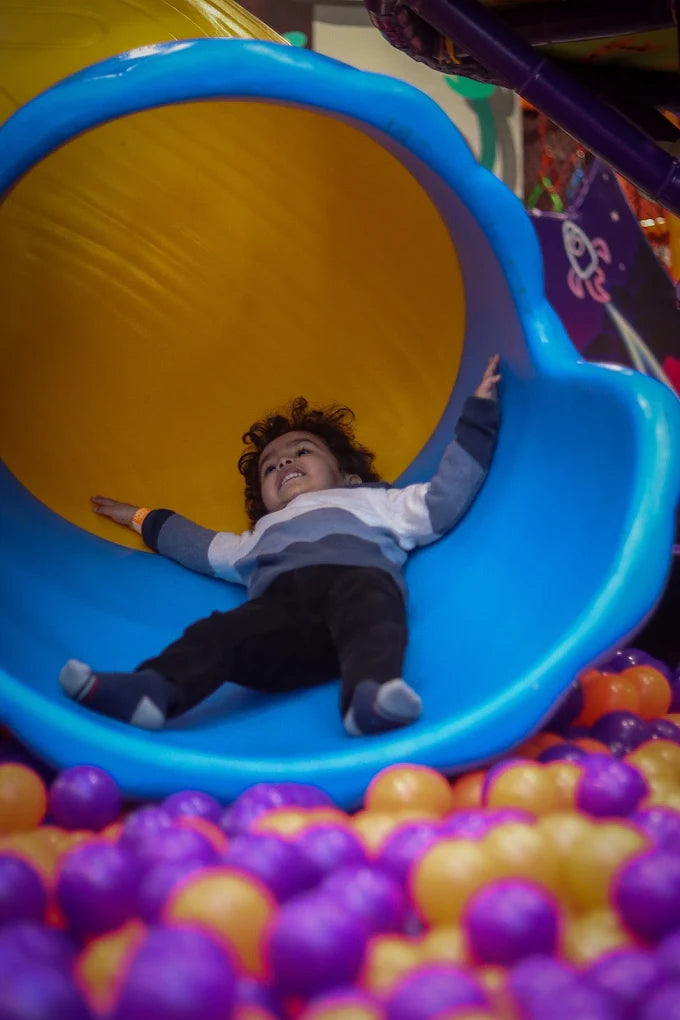 Child sliding down vibrant blue and yellow slide into colorful ball pit at Fun Orbbit Kids Play Area Gujranwala Town Delhi