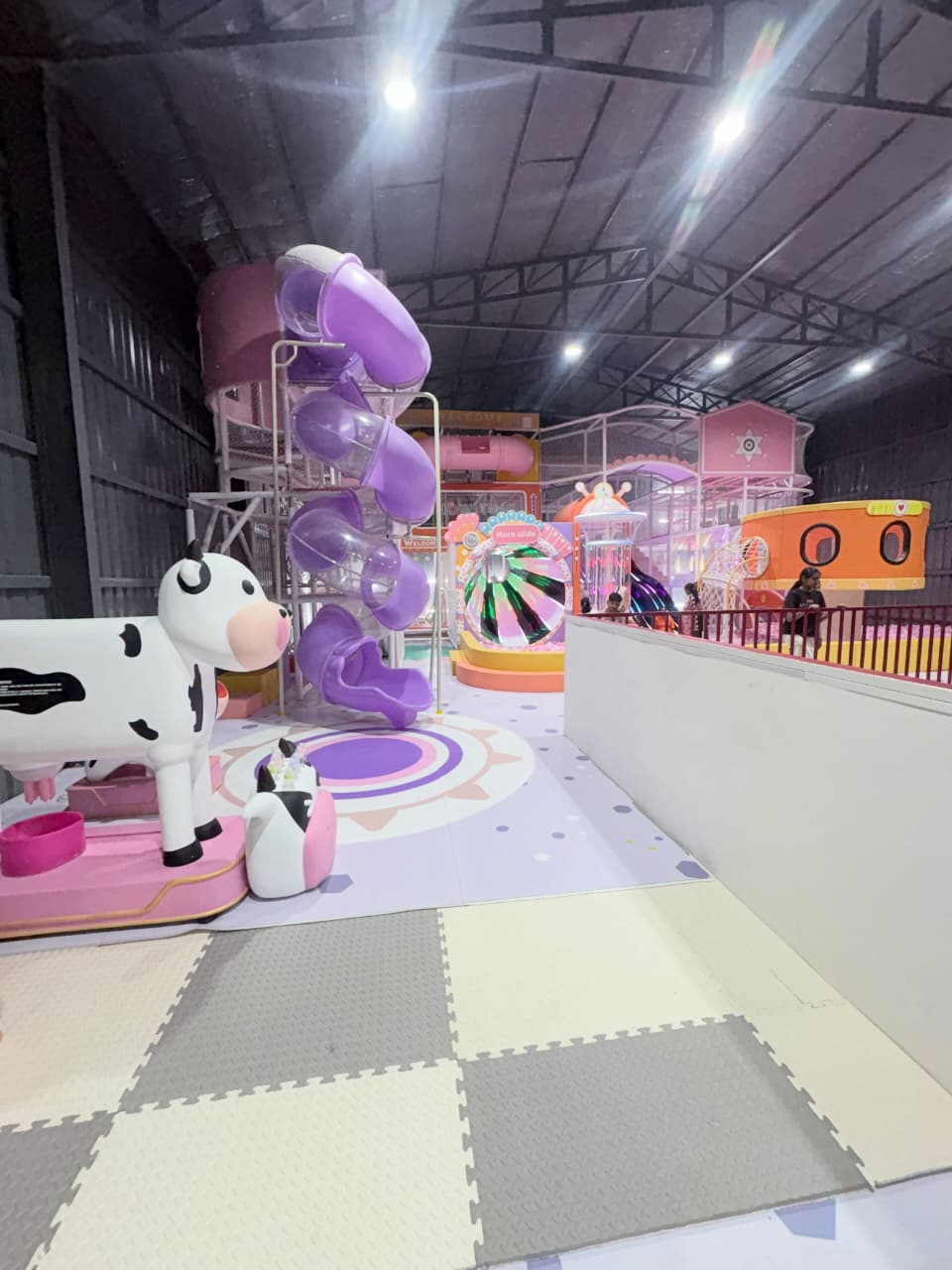 A colorful indoor playground with purple slides and a cow-themed play area for children.
