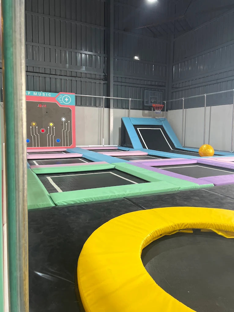 An indoor trampoline park with multiple trampolines and a basketball hoop.