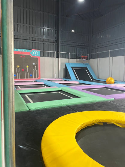 An indoor trampoline park with multiple trampolines and a basketball hoop.