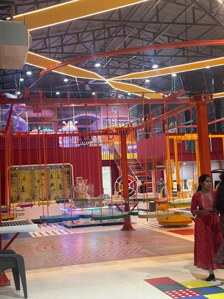 An indoor adventure park with rope courses, swings, and a slide, with young people enjoying the activities.