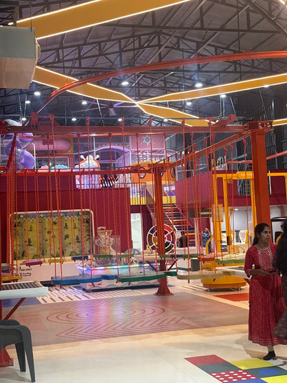 An indoor adventure park with rope courses, swings, and a slide, with young people enjoying the activities.
