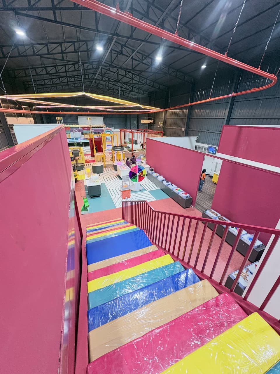 A colorful indoor play area with children exploring exhibits, viewed from a vibrant, cushioned staircase.