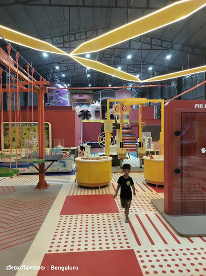 A young boy walks through a colorful indoor play area with yellow lights overhead.