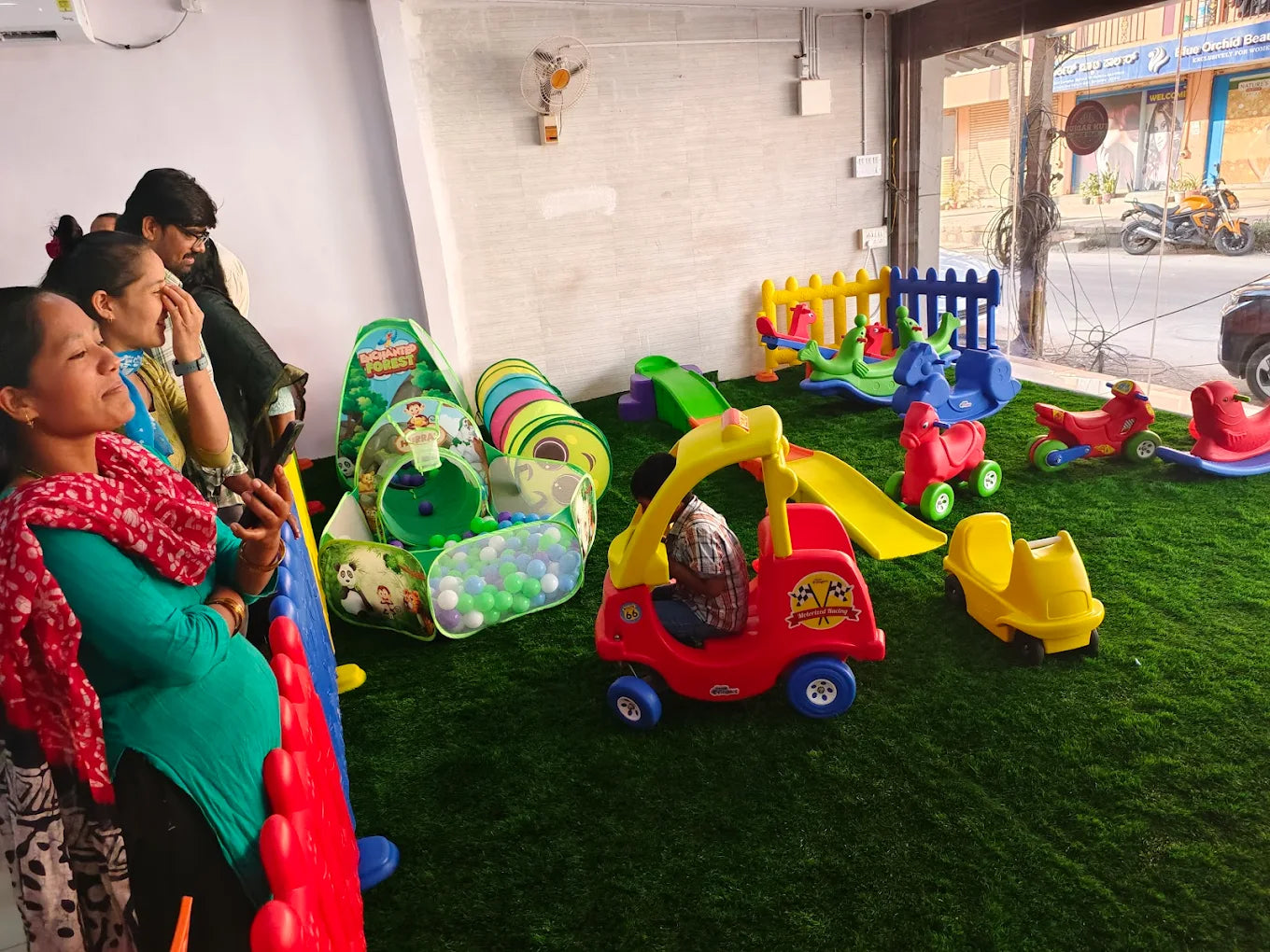 Children playing in a colorful indoor playground with slides, ball pits, and ride-on toys.
