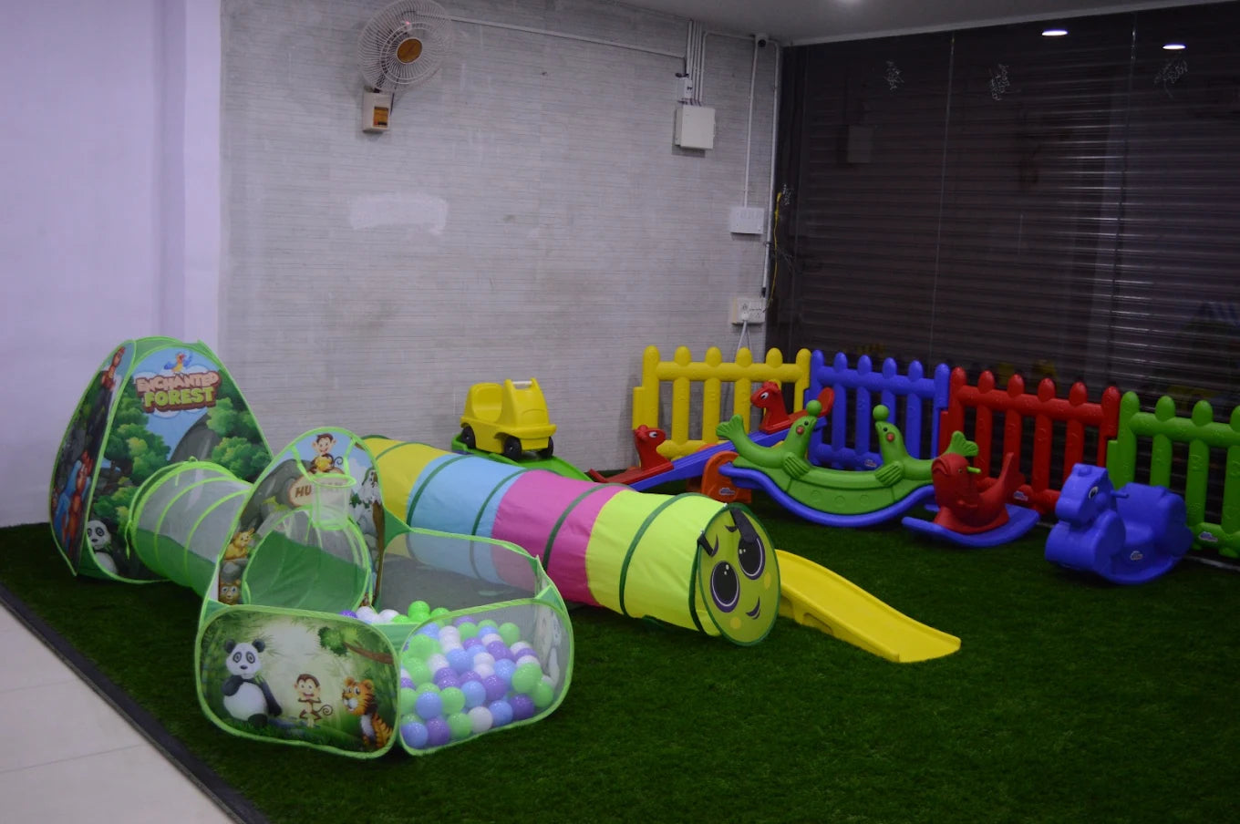 A colorful indoor play area for young children with tunnels, a ball pit, and rocking toys.
