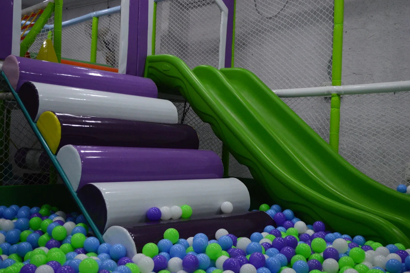 A colorful ball pit with a green slide and padded steps in a children's play area.