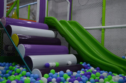 A colorful ball pit with a green slide and padded steps in a children's play area.