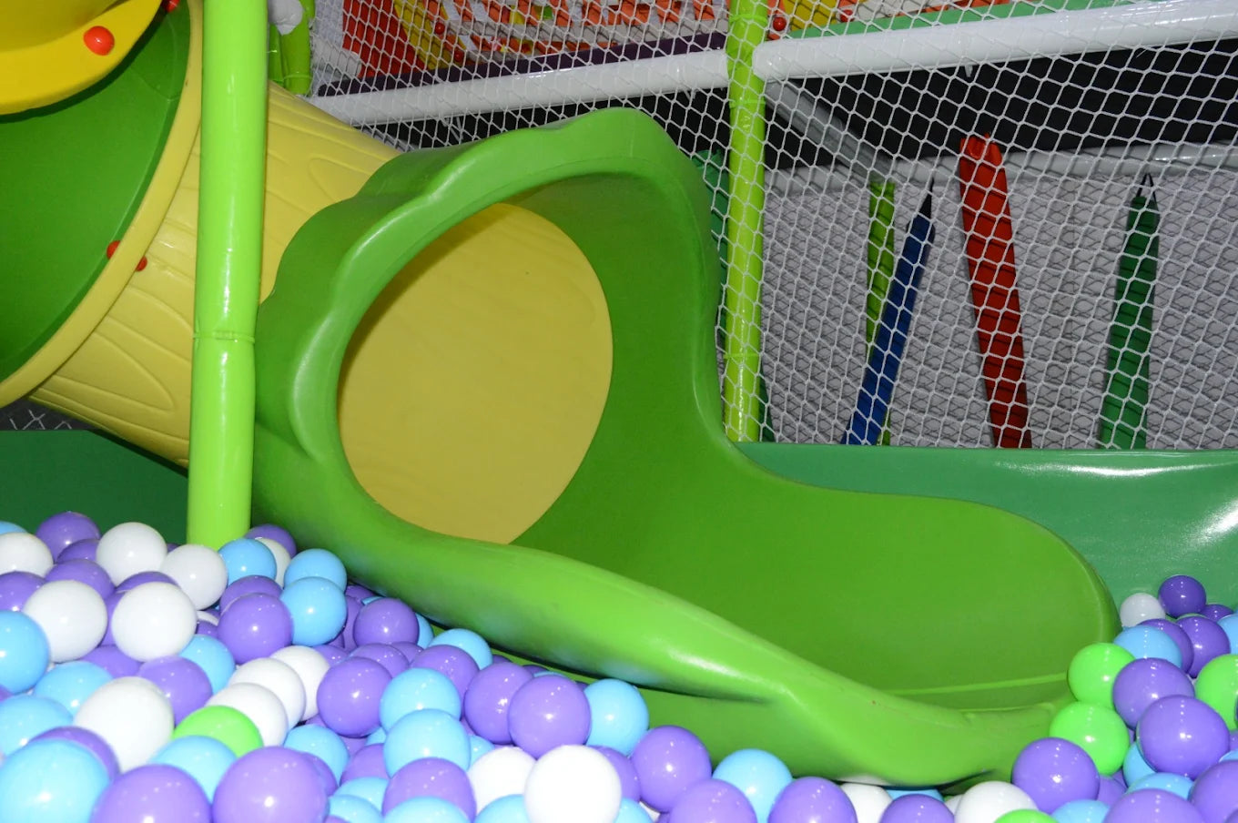 A colorful ball pit with a green slide in a children's play area.