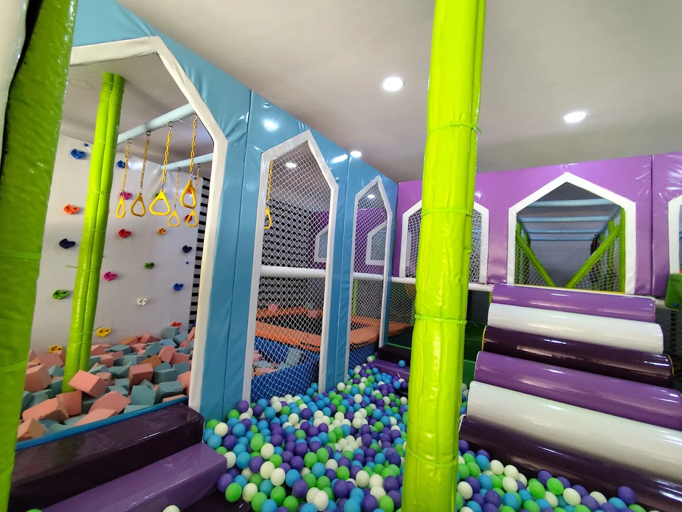 A colorful indoor playground with a ball pit, foam blocks, and climbing rings for children.