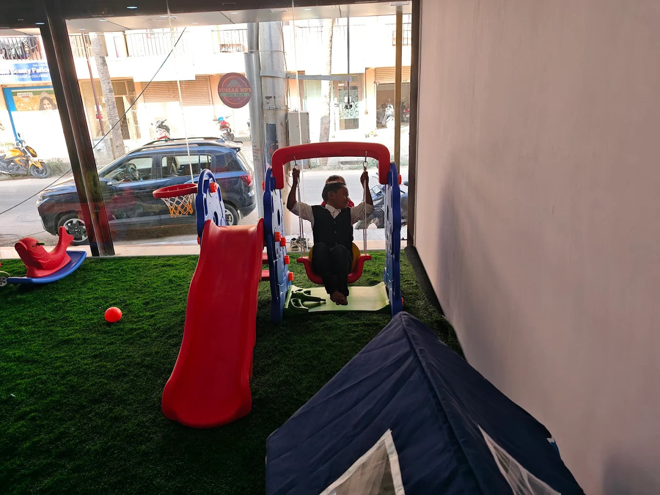 A child swings on a playground swing set next to a slide, with a tent in the foreground.