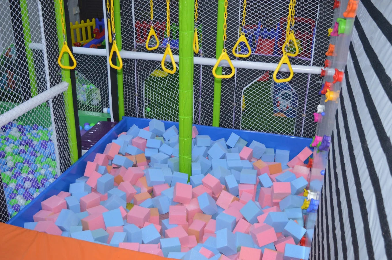 A colorful indoor playground with a foam pit and hanging rings for children.