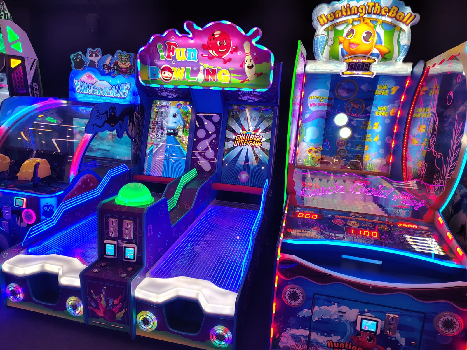 Arcade games with bright neon lights, including bowling and fishing games, are set up in a dimly lit entertainment center.