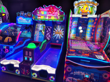 Arcade games with bright neon lights, including bowling and fishing games, are set up in a dimly lit entertainment center.