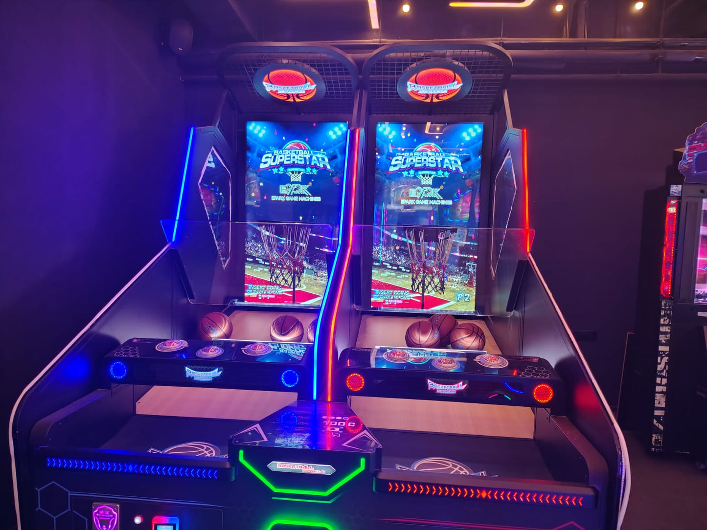 Two arcade basketball games are set up side-by-side in a dimly lit entertainment venue.